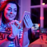chica sosteniendo un móvil con una luz purpúrea en una habitación